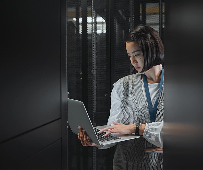 person looking at a laptop behind a server rack
