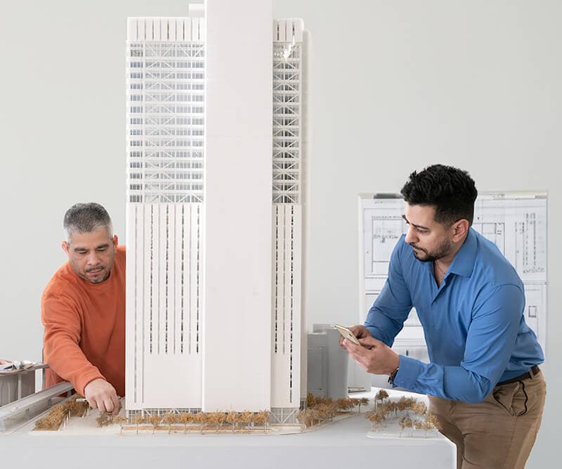 Two architects discussing a physical model of a high-rise in an office setting