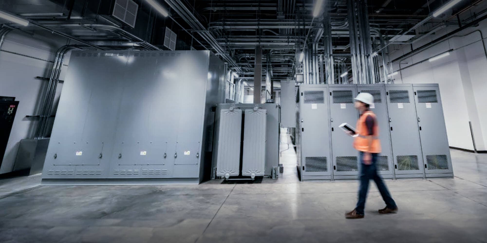 Worker in hard hat and safety vest and a tablet walking through a data center