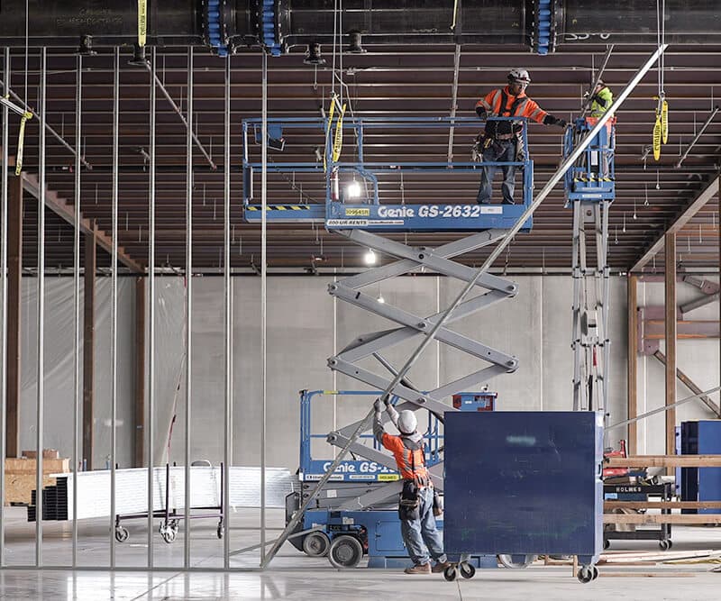Construction workers in a warehouse using a scissor lift