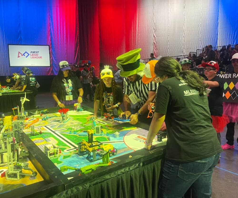 Team of middle school students and two referees inspecting robots on a table at a competition