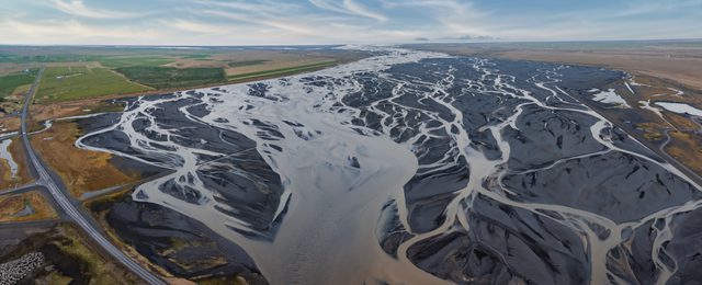 A stunning aerial view of a light blue river delta in Iceland, showcasing a complex network of waterways against a dark gray landscape. Unique natural beauty.