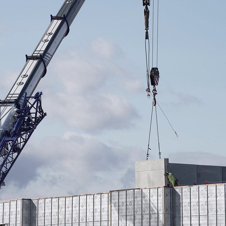 Crane lowering a large concrete slab into a construction site with a worker guiding it