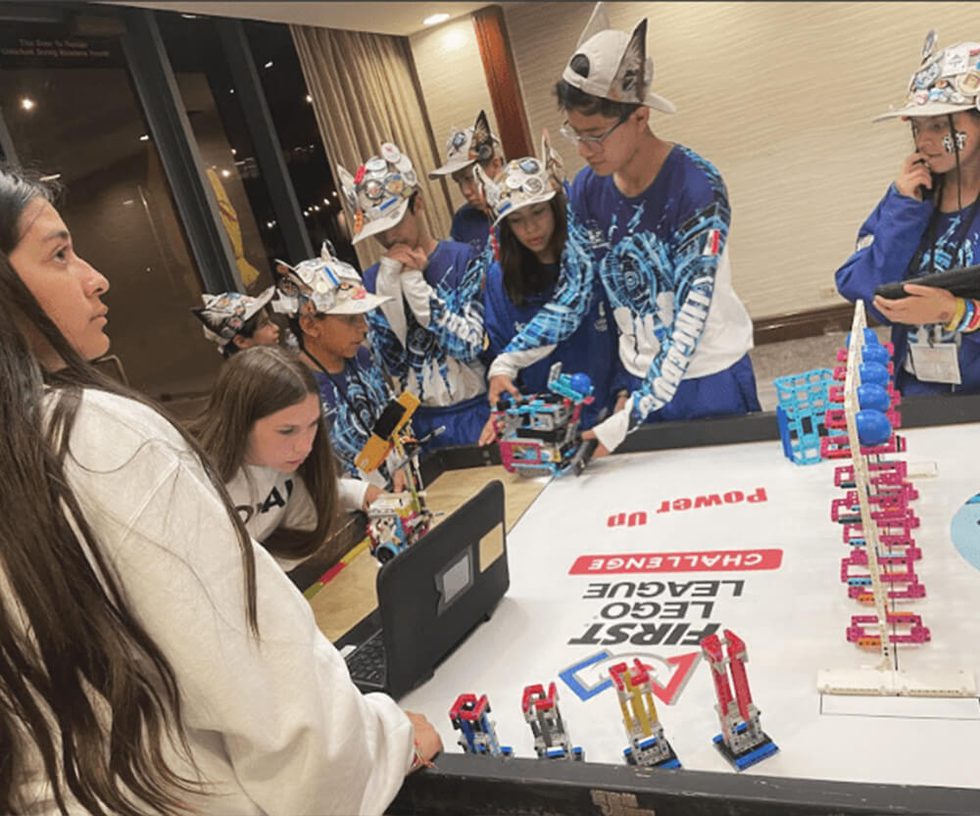 Team of middle school students working together at a table with Lego robots