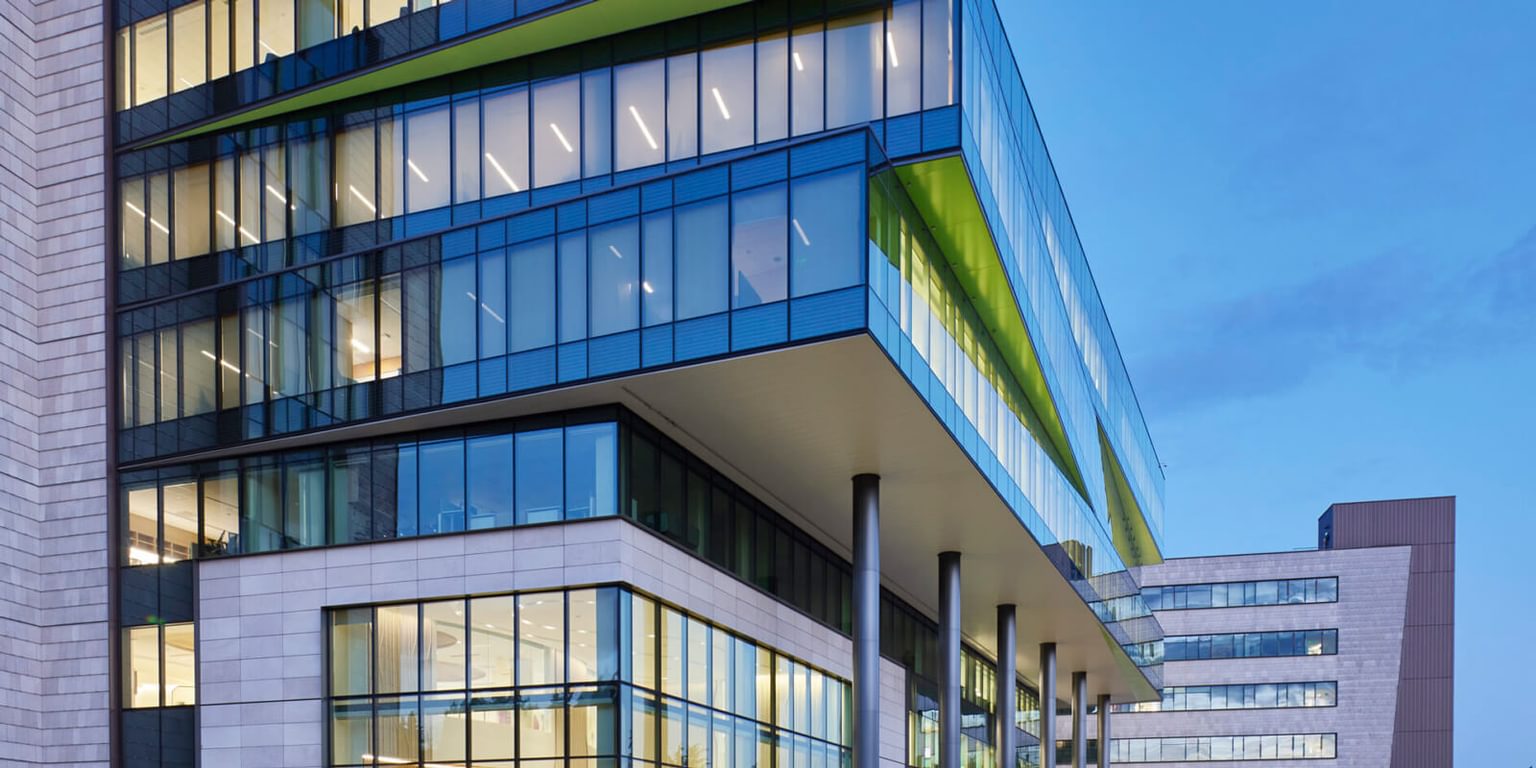 The corner of a large building with tall windows and a blue sky in the background.