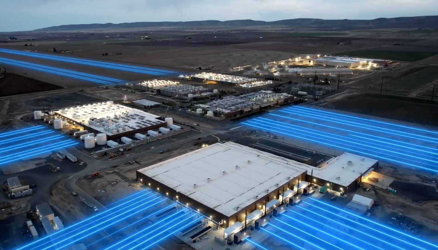 A drone shot of data centers with blue lights trailing from the buildings.