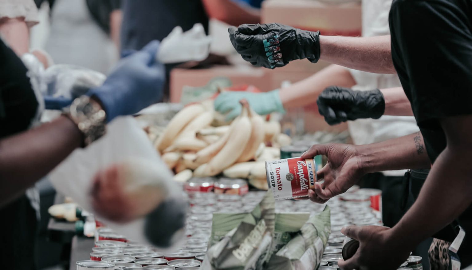 People working at a food drive showing a hand holding a Campbell's soup can and produce in the background.