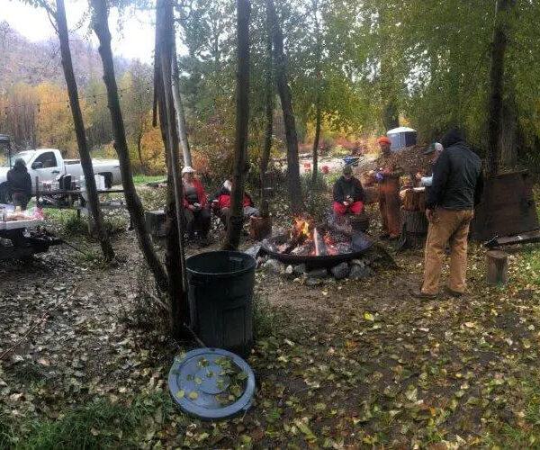 Workers at a camp site with a fire pit in the center and a truck in the far distance.